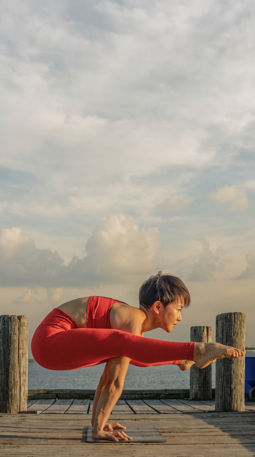 Julia Lee holding an arm balance on a dock under a cloudy sky